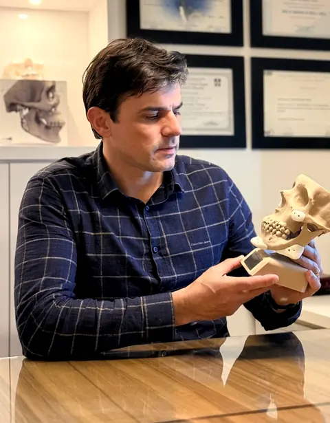 Dr. Samir Veran mostrando um modelo 3D de crânio com placas de fixação